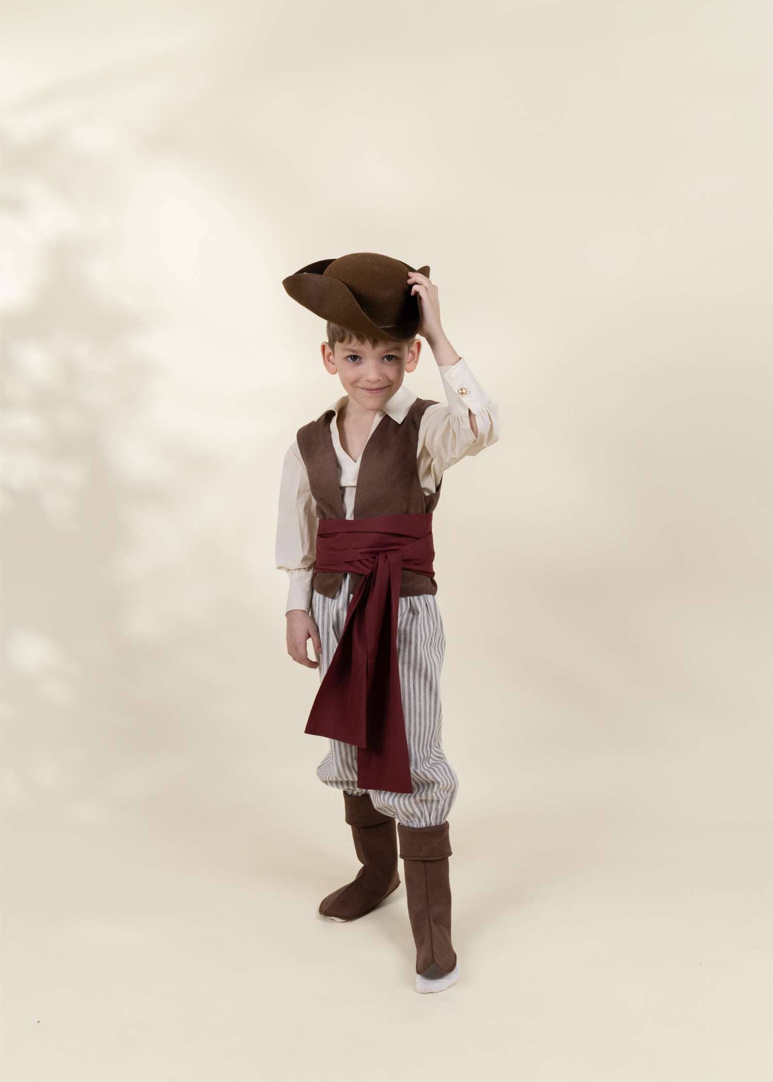Child wearing a pirate costume with a vest, shirt, pants, and hat on a light background
