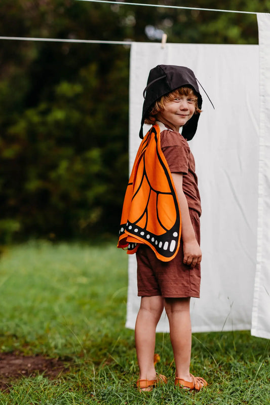 Child wearing a butterfly costume standing outdoors with a white sheet in the background