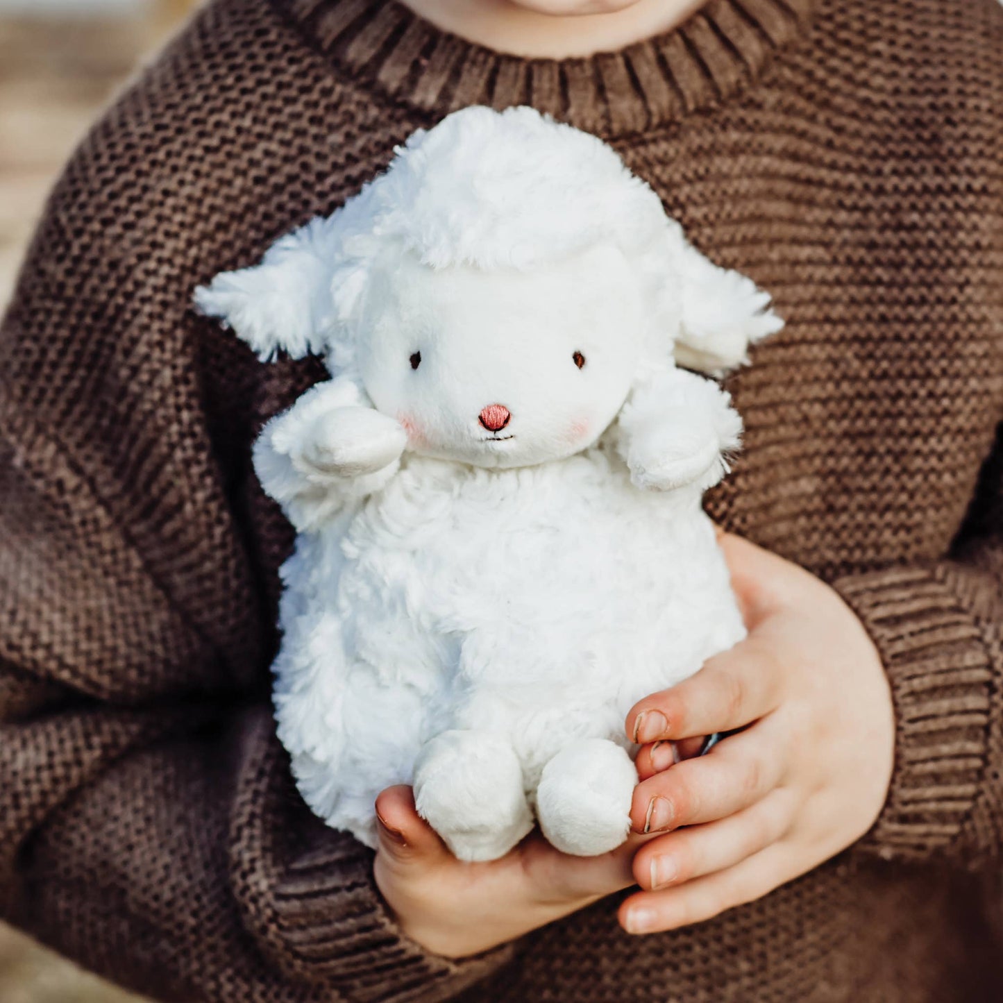 Person holding a white fluffy toy in a brown sweater