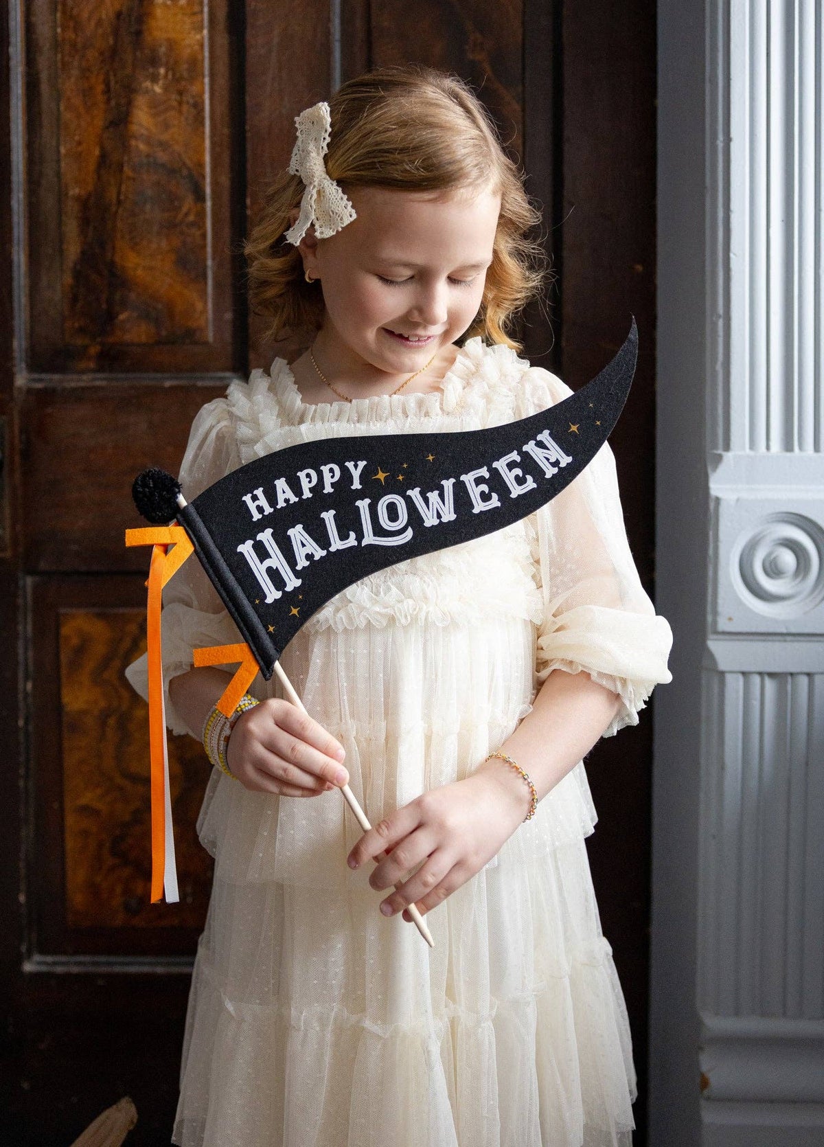 Young girl in a white dress holding a 'Happy Halloween' banner.