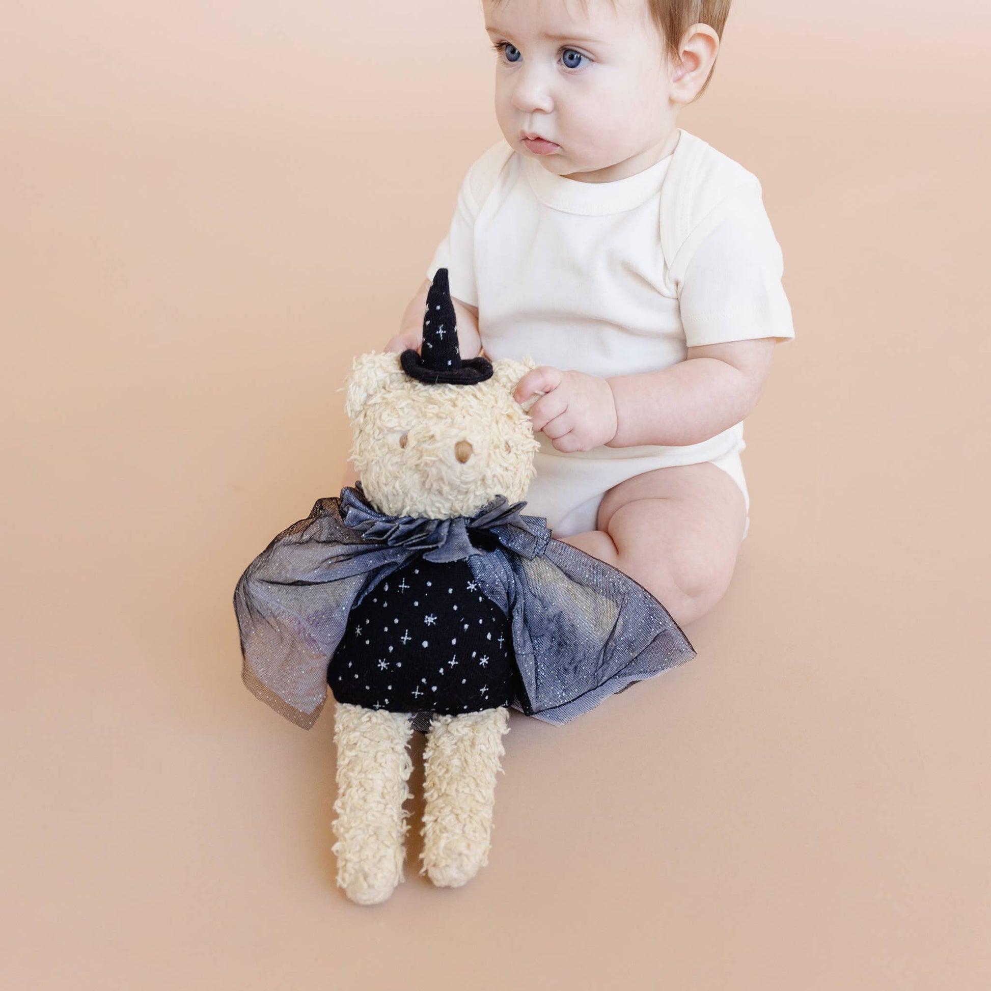 Baby sitting next to a teddy bear dressed as a unicorn on a beige background