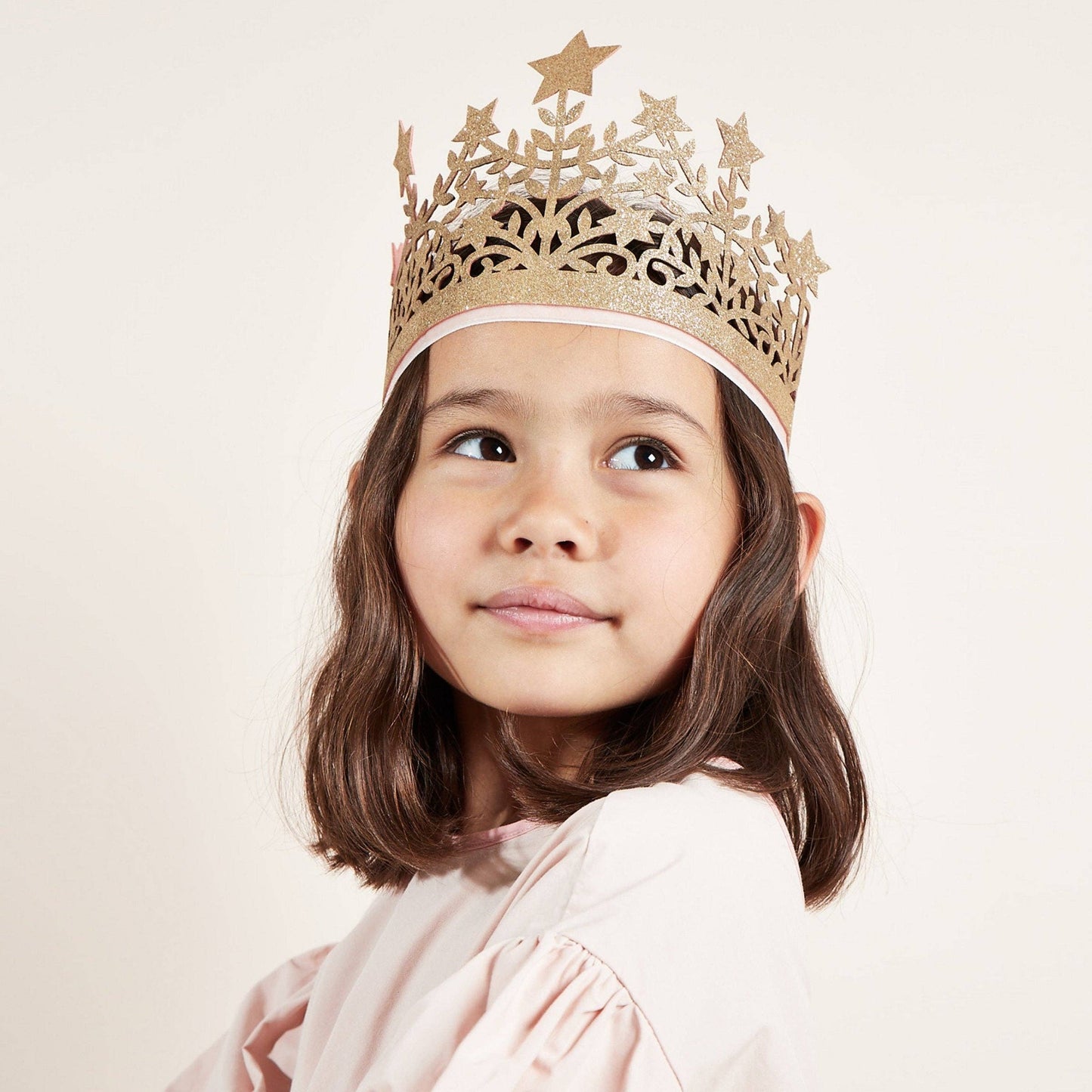 Young girl wearing a gold decorative crown on a plain background