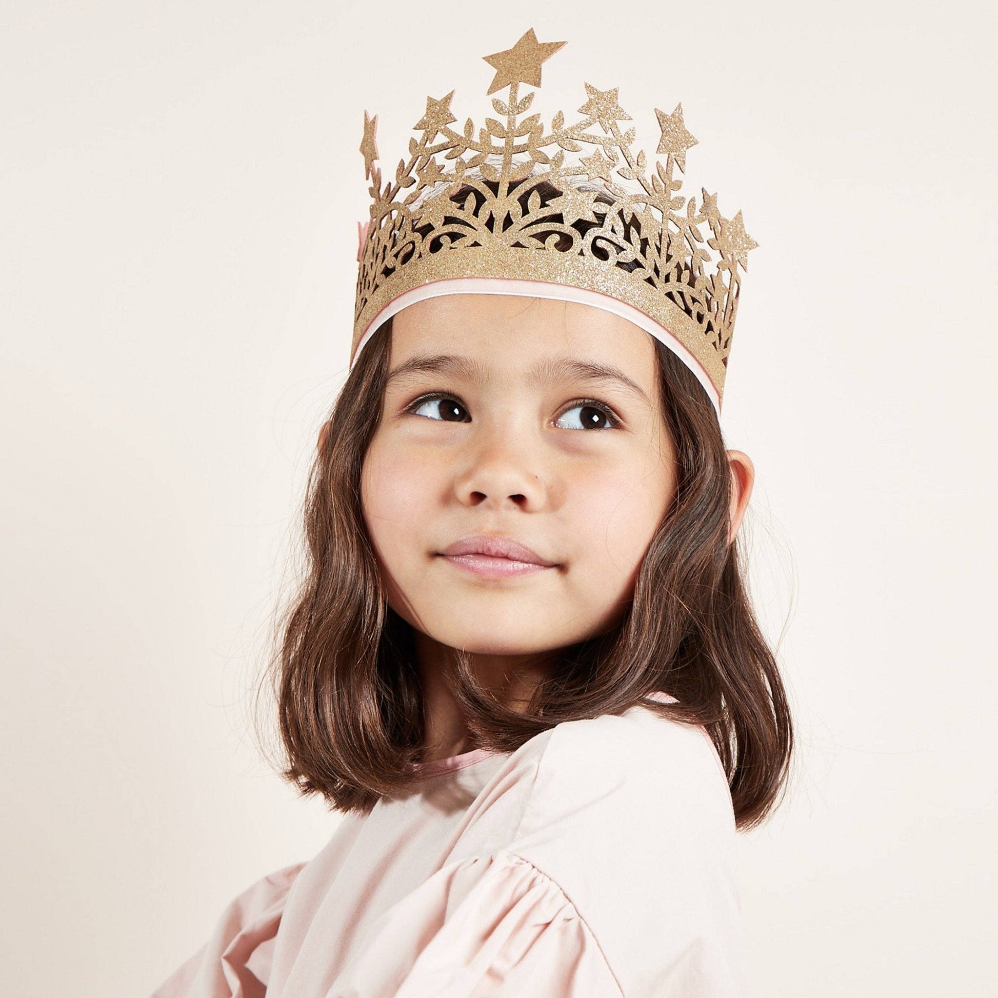 Young girl wearing a gold decorative crown on a plain background
