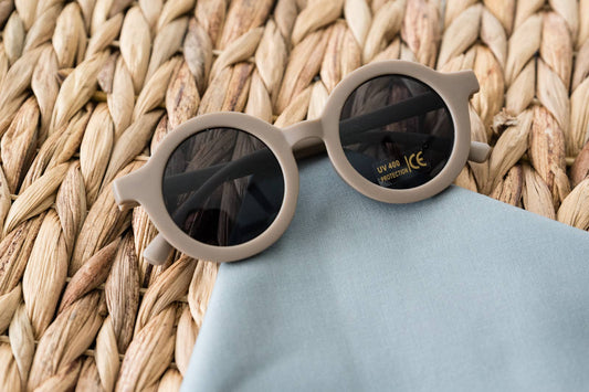 A pair of beige retro sunglasses with a smooth and lustrous design, placed on a textured surface next to a blue cloth.