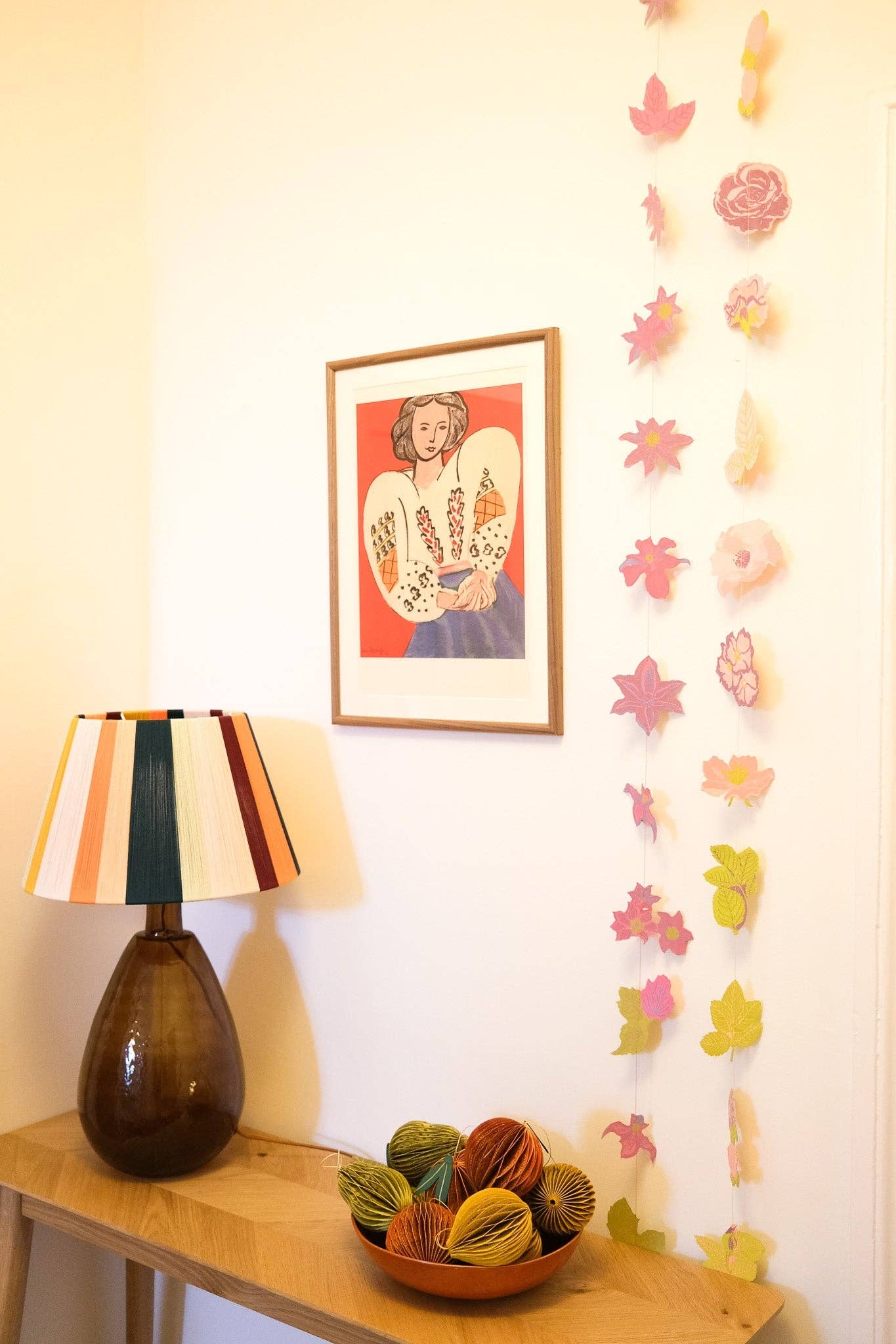 Decorative lamp on a table with a colorful abstract painting and wall garlands in the background.