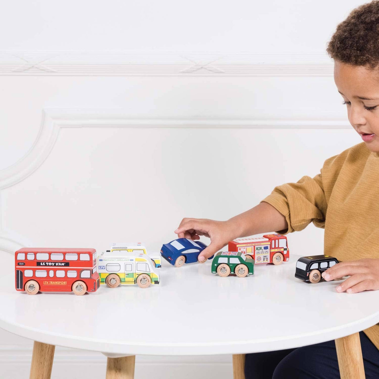 Child playing with wooden toy cars on a white table
