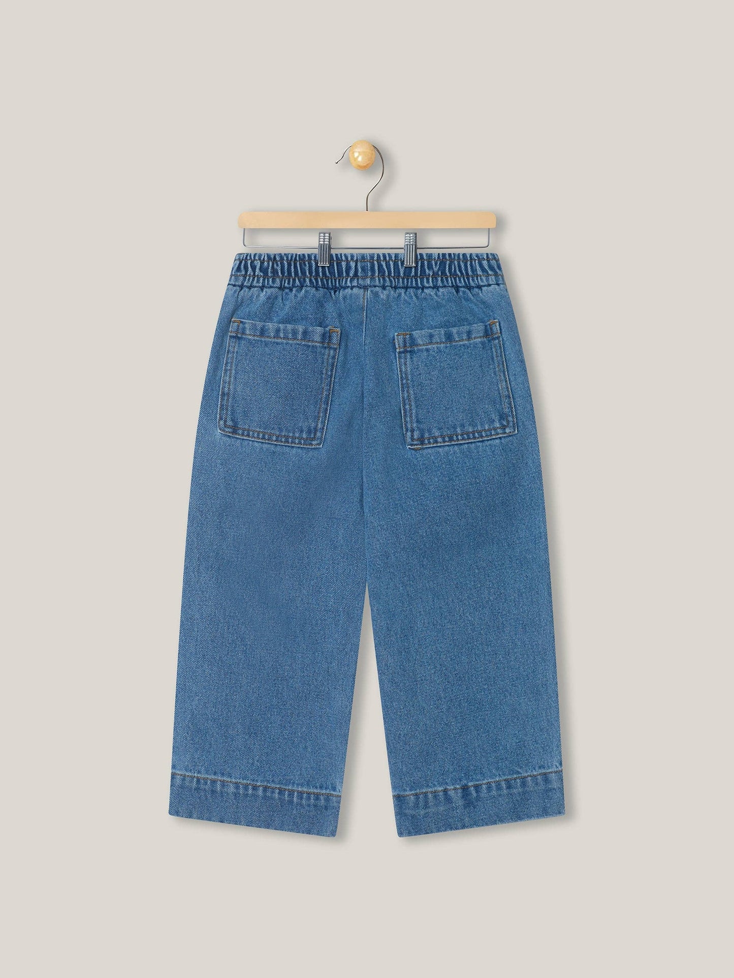 Back view of blue denim pants on a hanger against a light gray background
