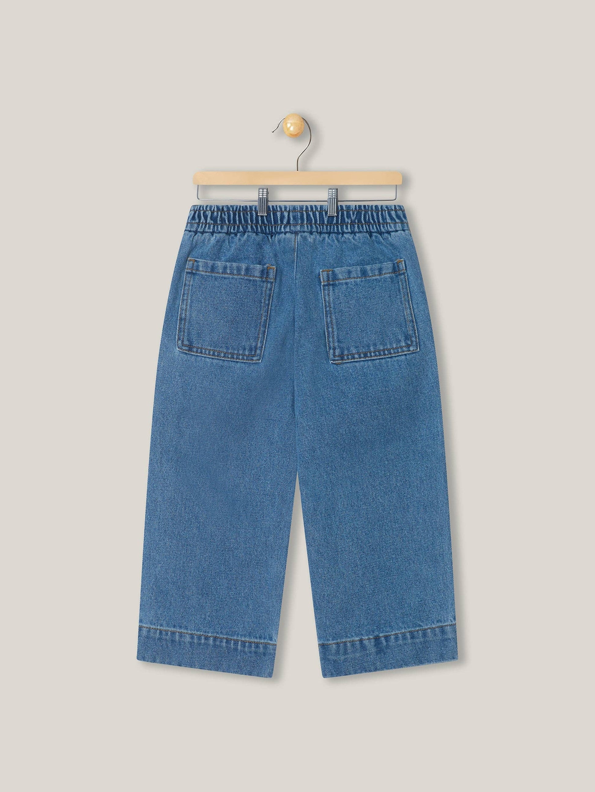 Back view of blue denim pants on a hanger against a light gray background