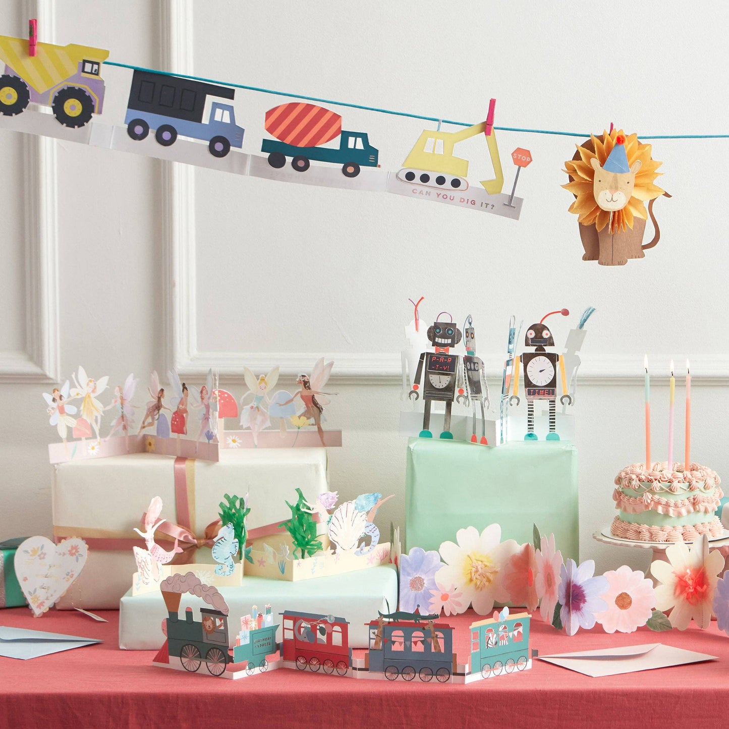 Children's birthday party setup with cake, decorations, and a banner featuring vehicles and animals.