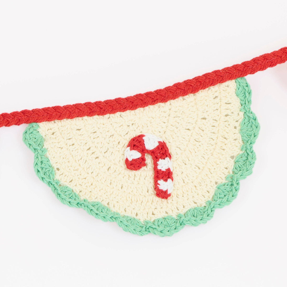 A crocheted Christmas bunting banner featuring a scalloped cream-colored half-circle panel with a green edge, a red top border, and a red-and-white candy cane motif in the center.