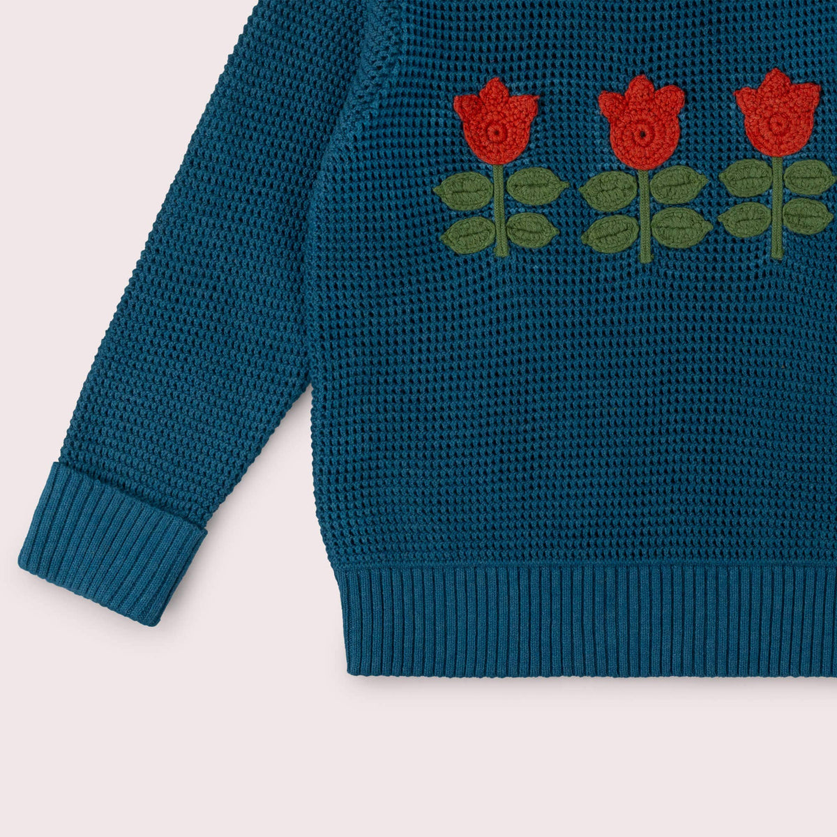 Detail of red tulips, green leaves, ribbed cuff and hem on a teal knitted jumper.