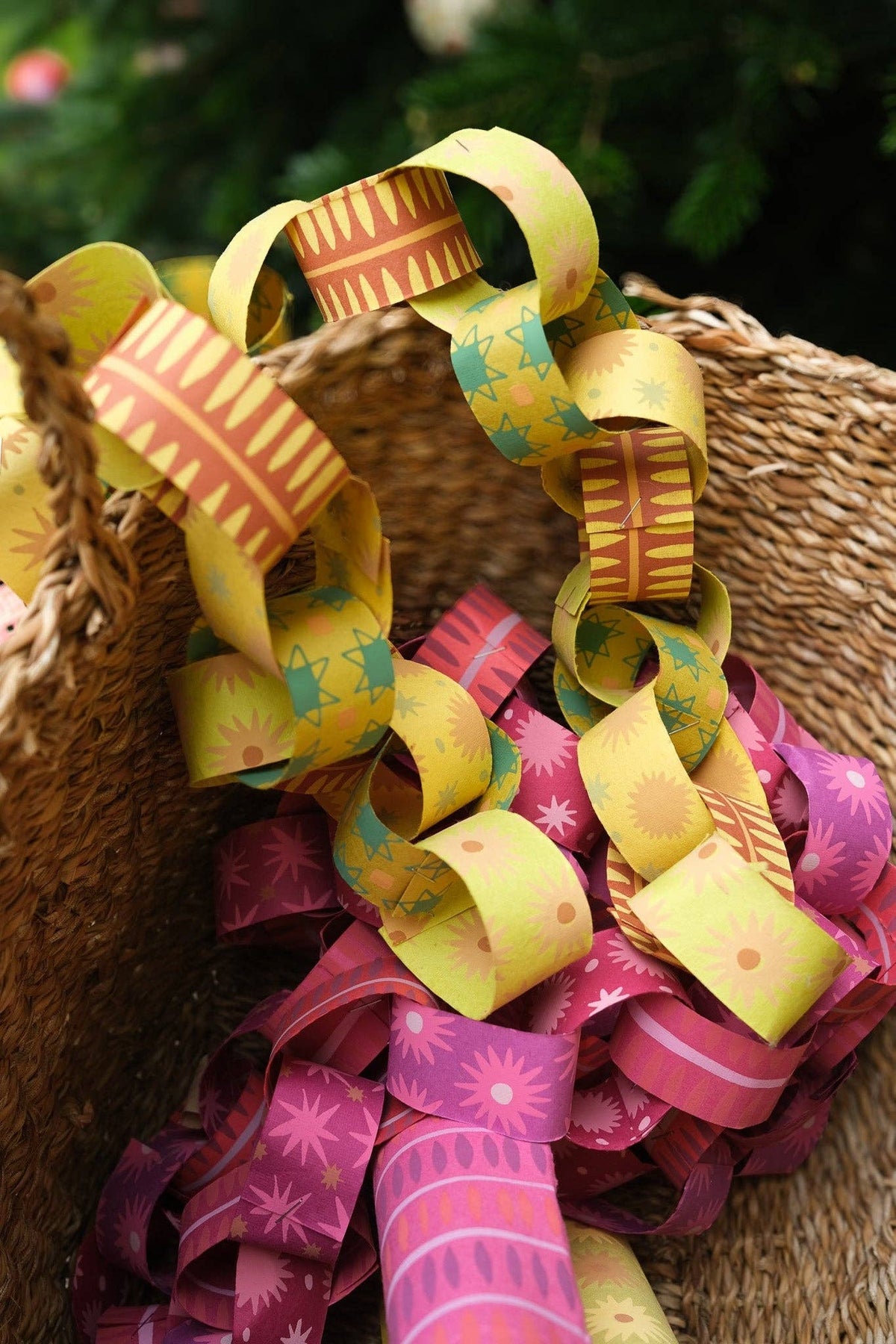 Yellow, green and orange patterned paper chains piled with pink paper chains in a woven basket.