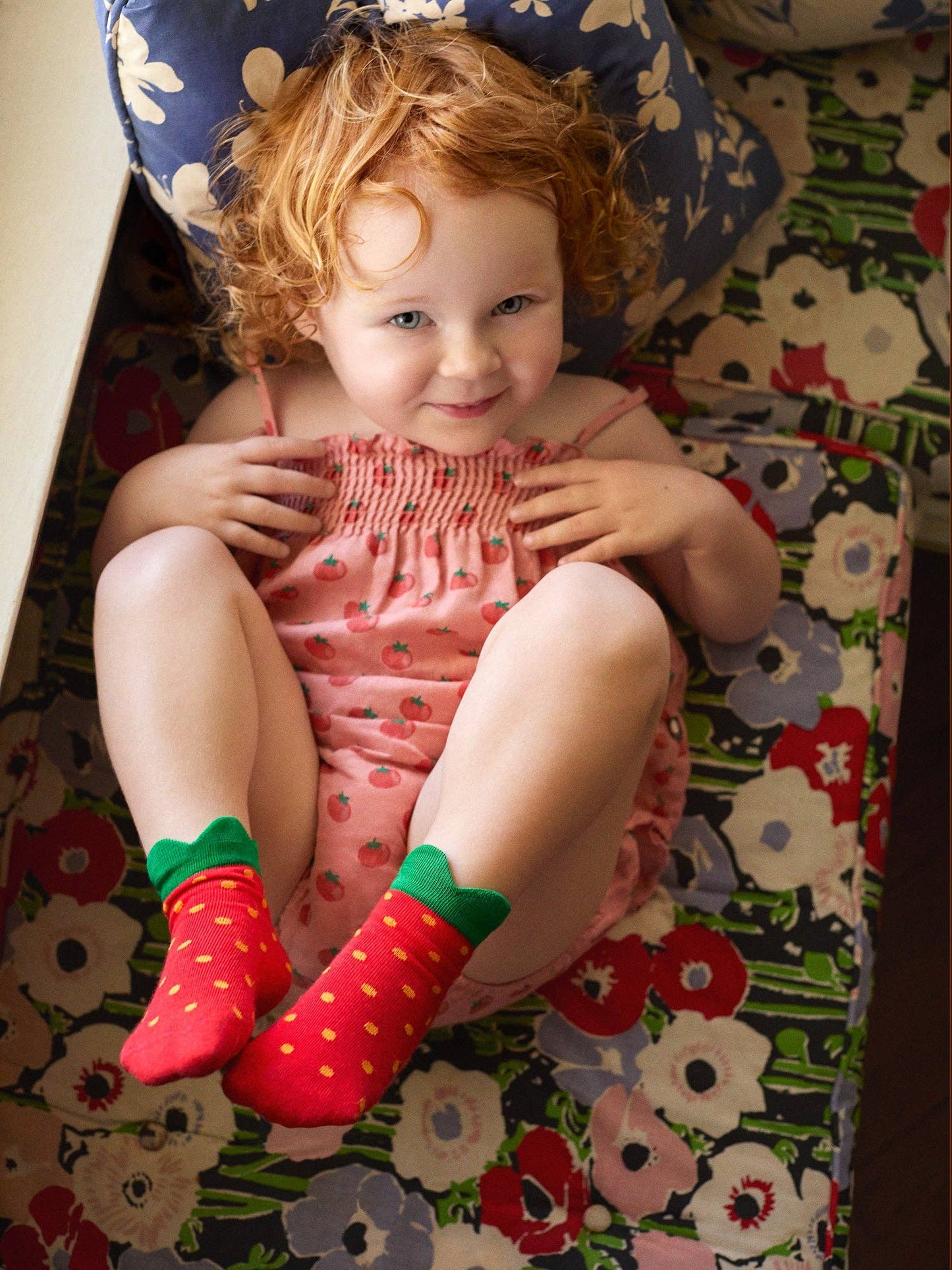 Child wearing red strawberry socks sitting on a floral-patterned surface