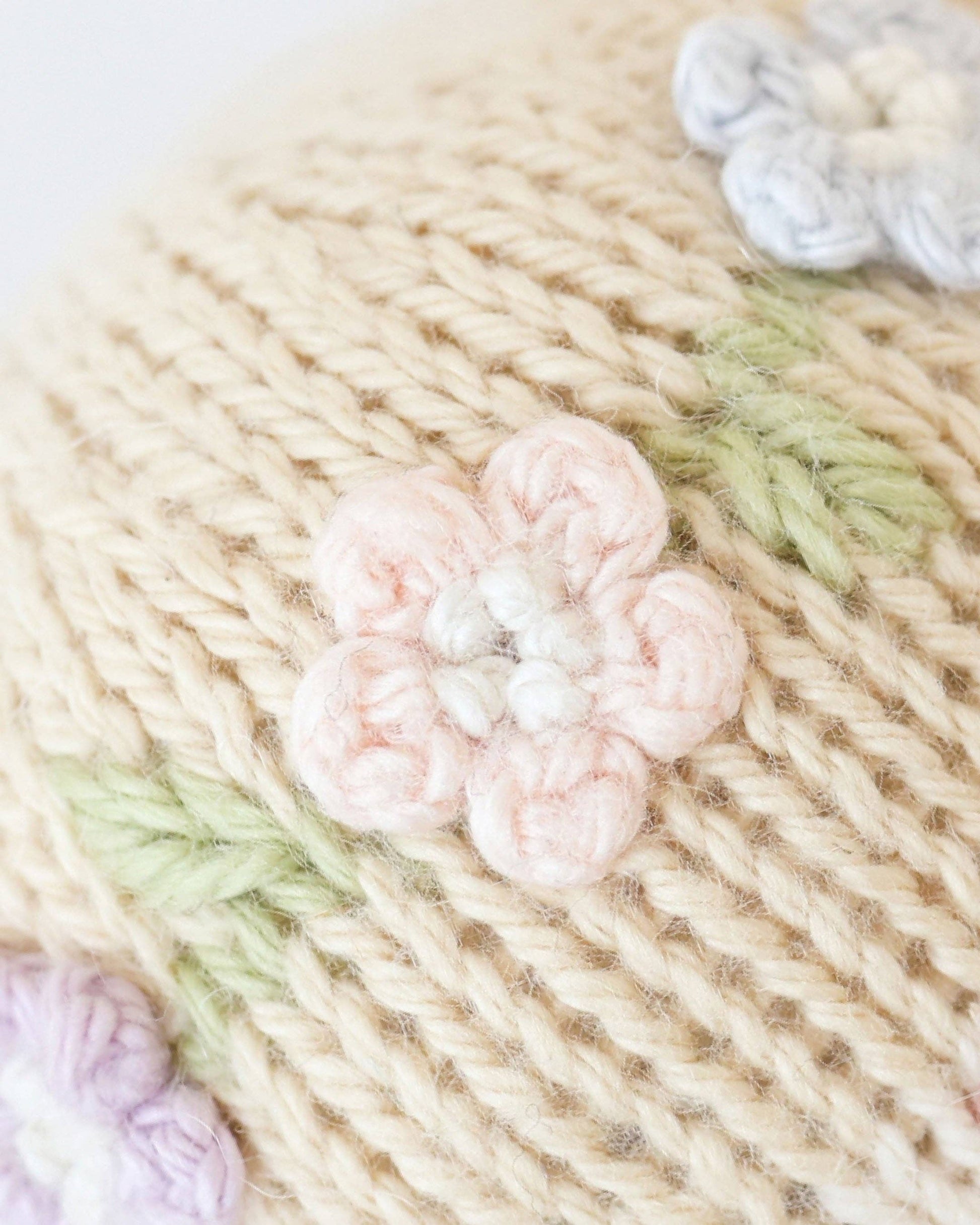 Close-up of knitted fabric with a pink flower design on a beige background