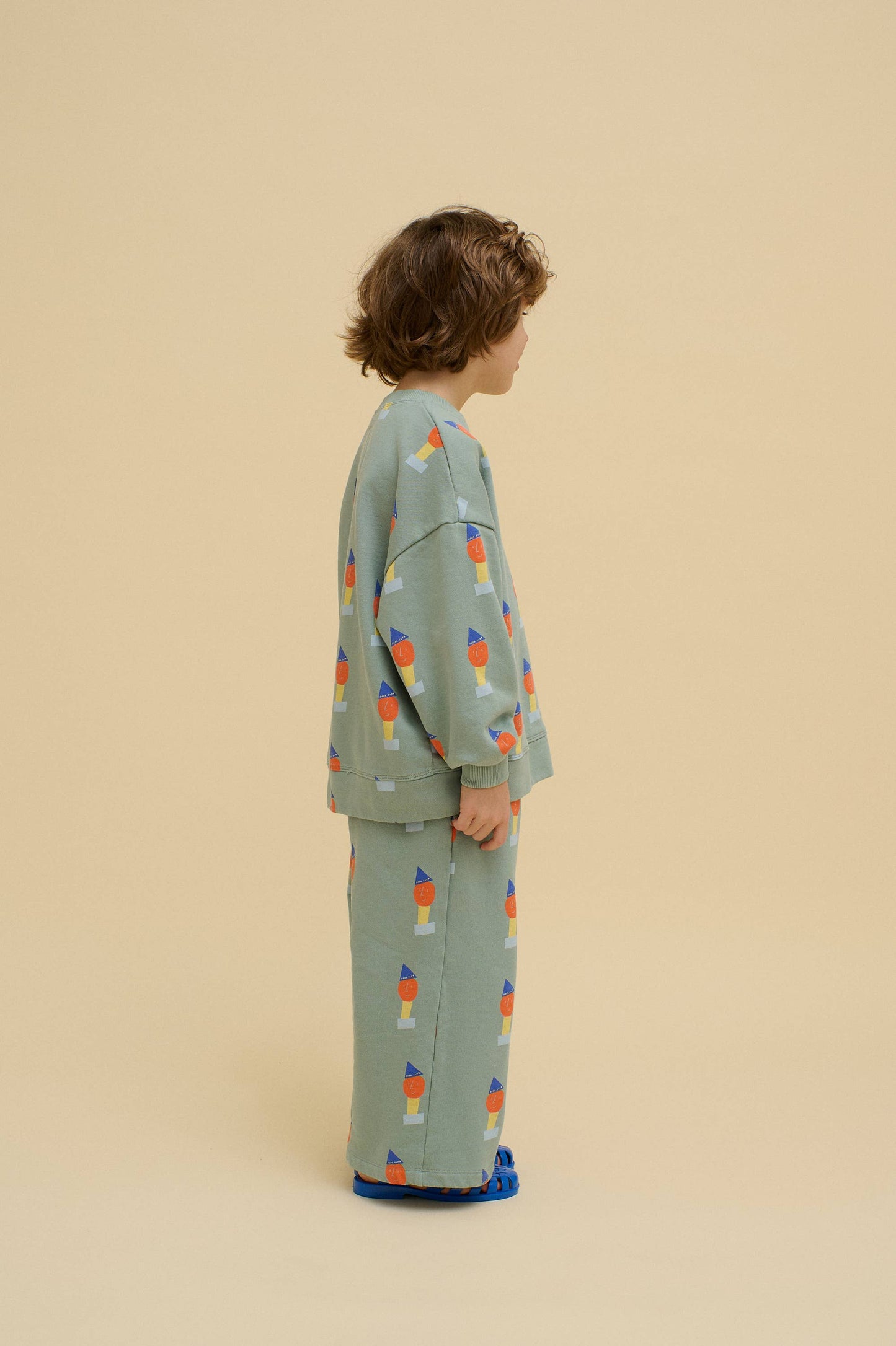 Child wearing a green pajama set with colorful designs on a beige background