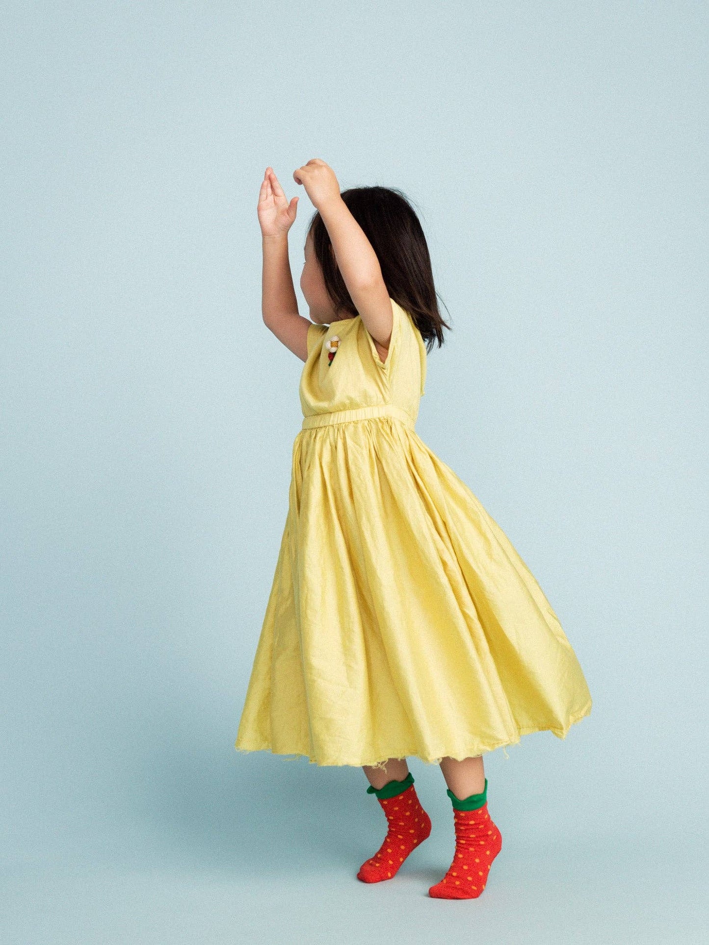 Child wearing a yellow dress with strawberry socks on a light blue background