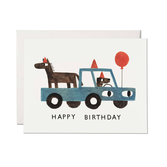 Happy Birthday card with an illustration of a dog driving a truck with a horse riding in the truck bed and a red balloon attached to the car