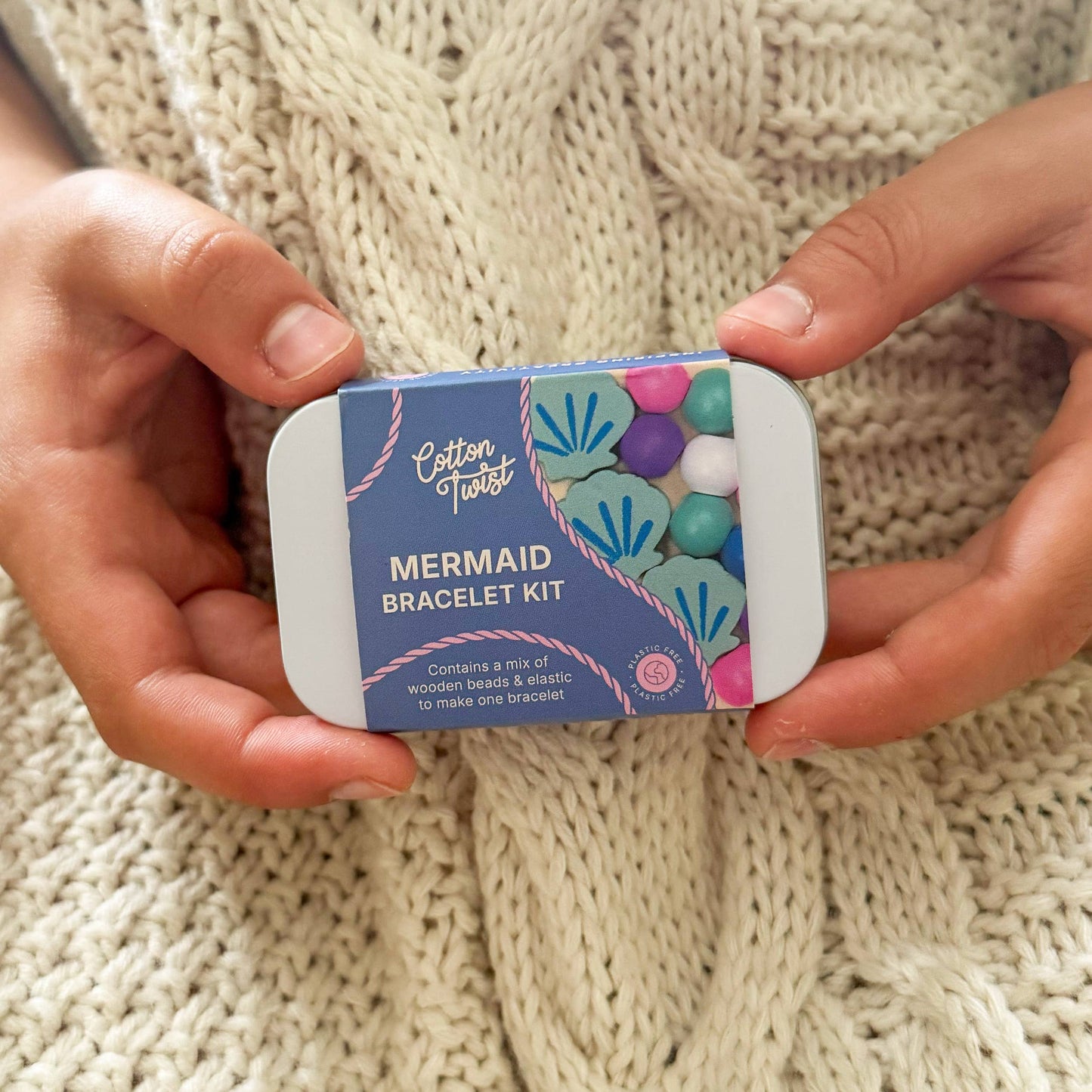 Mermaid bracelet kit packaging held by hands on a knitted fabric background