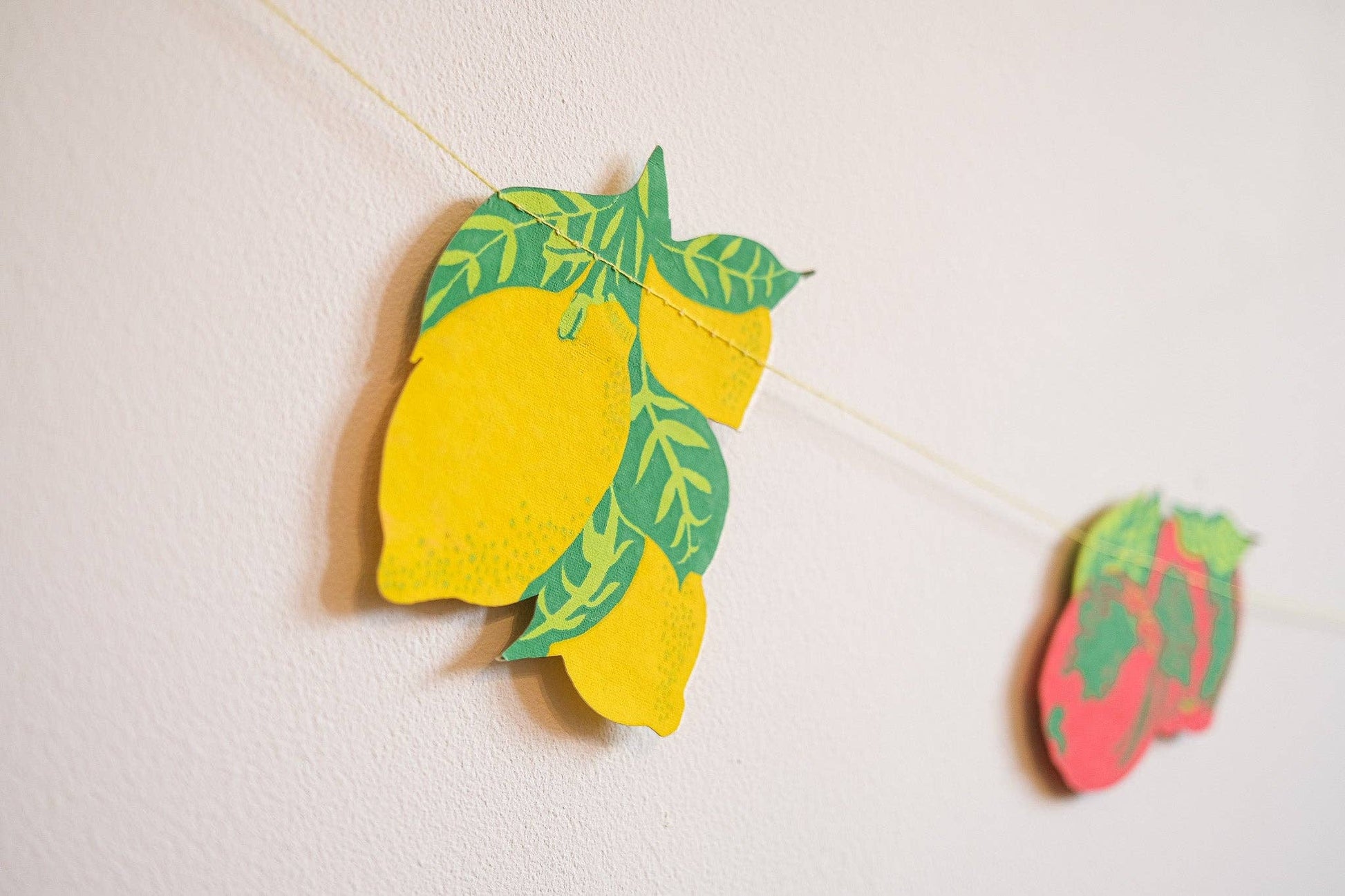 Decorative lemon and strawberry cutouts on a string against a light background