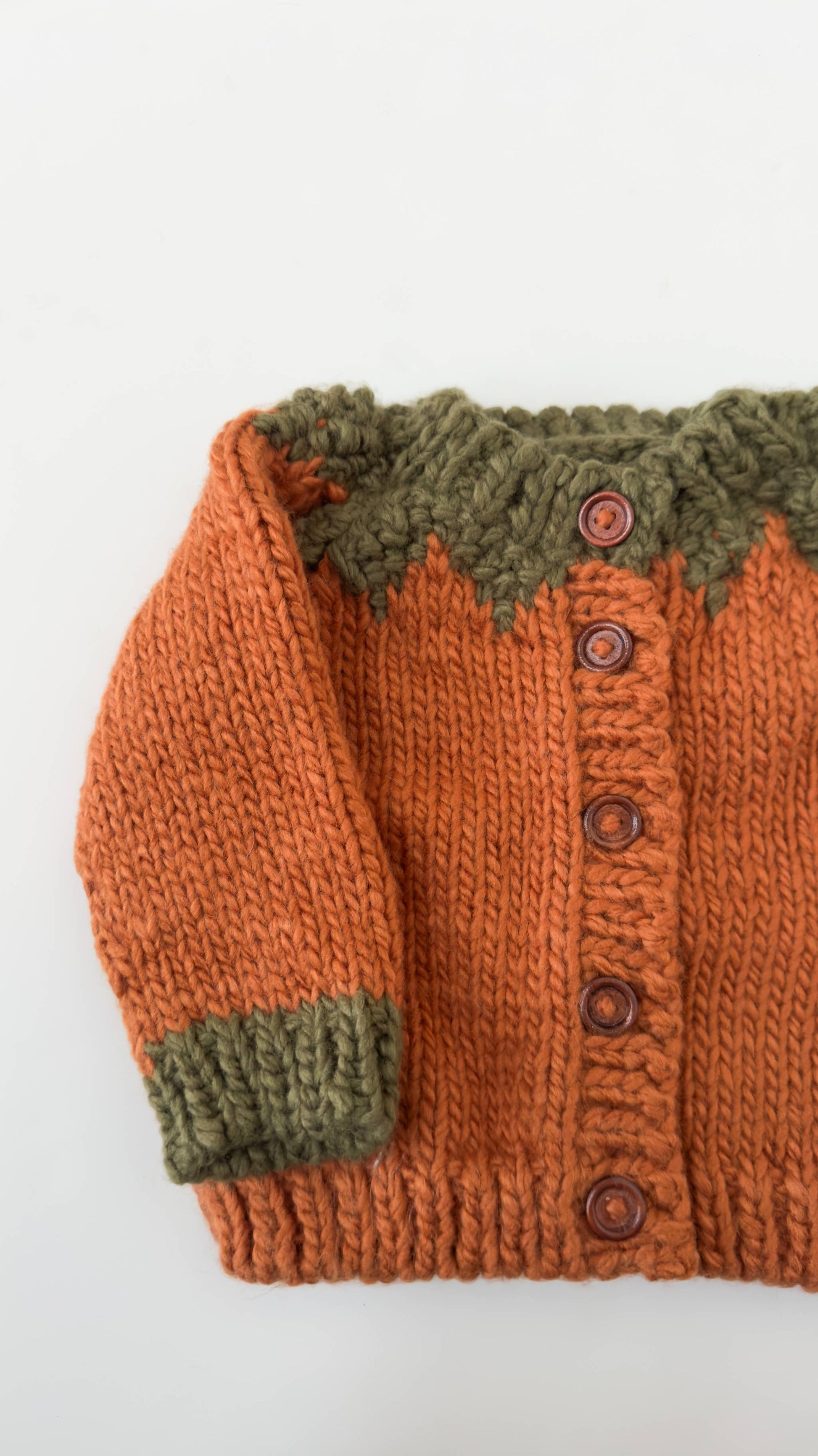 Knitted cardigan with orange body and green trim on a white background