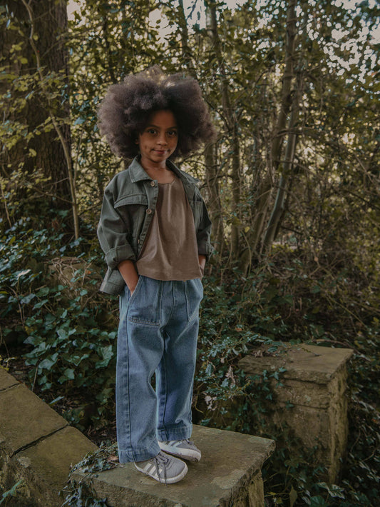 Child standing in a forest with trees and greenery in the background