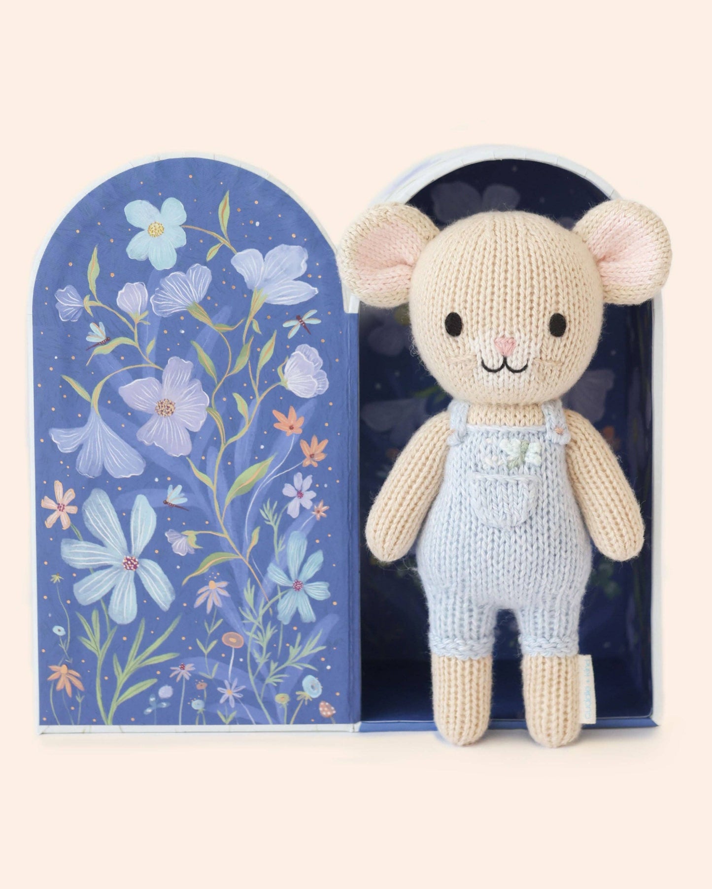 Knitted mouse toy in overalls standing next to a decorative box with floral patterns on a white background