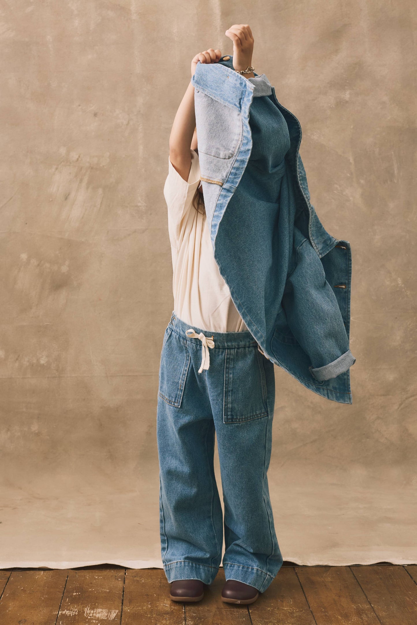 Child wearing a denim outfit against a beige wall