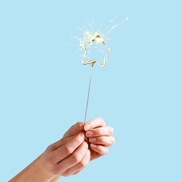 Hand holding a star-shaped sparkler against a light blue background