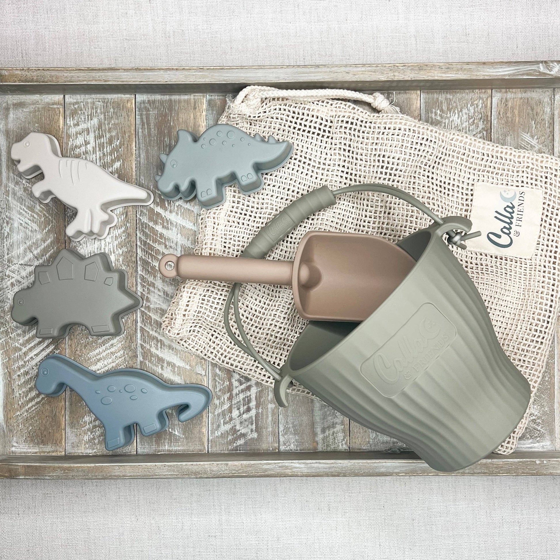 Children's toy set with dinosaur-shaped molds and a sand pail on a wooden surface.
