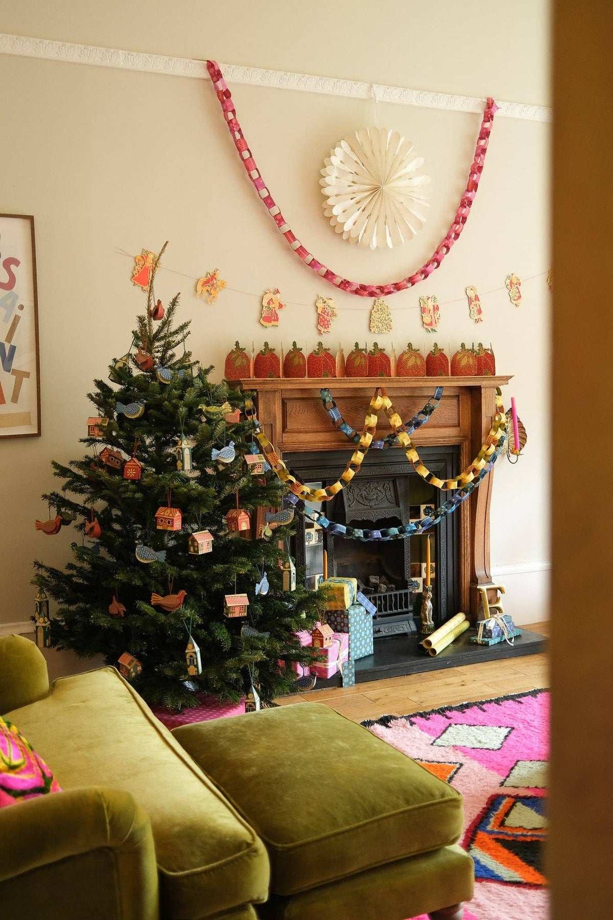 Christmas living room with pink, yellow and blue paper chains around the fireplace beside a decorated tree.