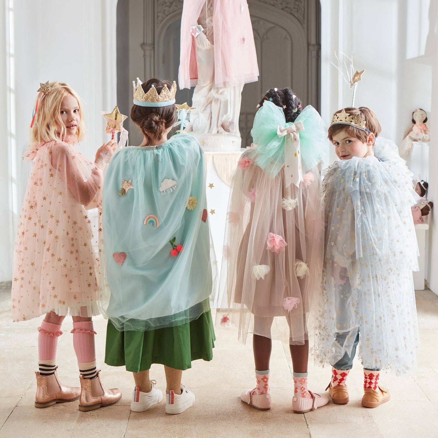 Four children in colorful costumes with fairy wings and crowns in a decorated room.