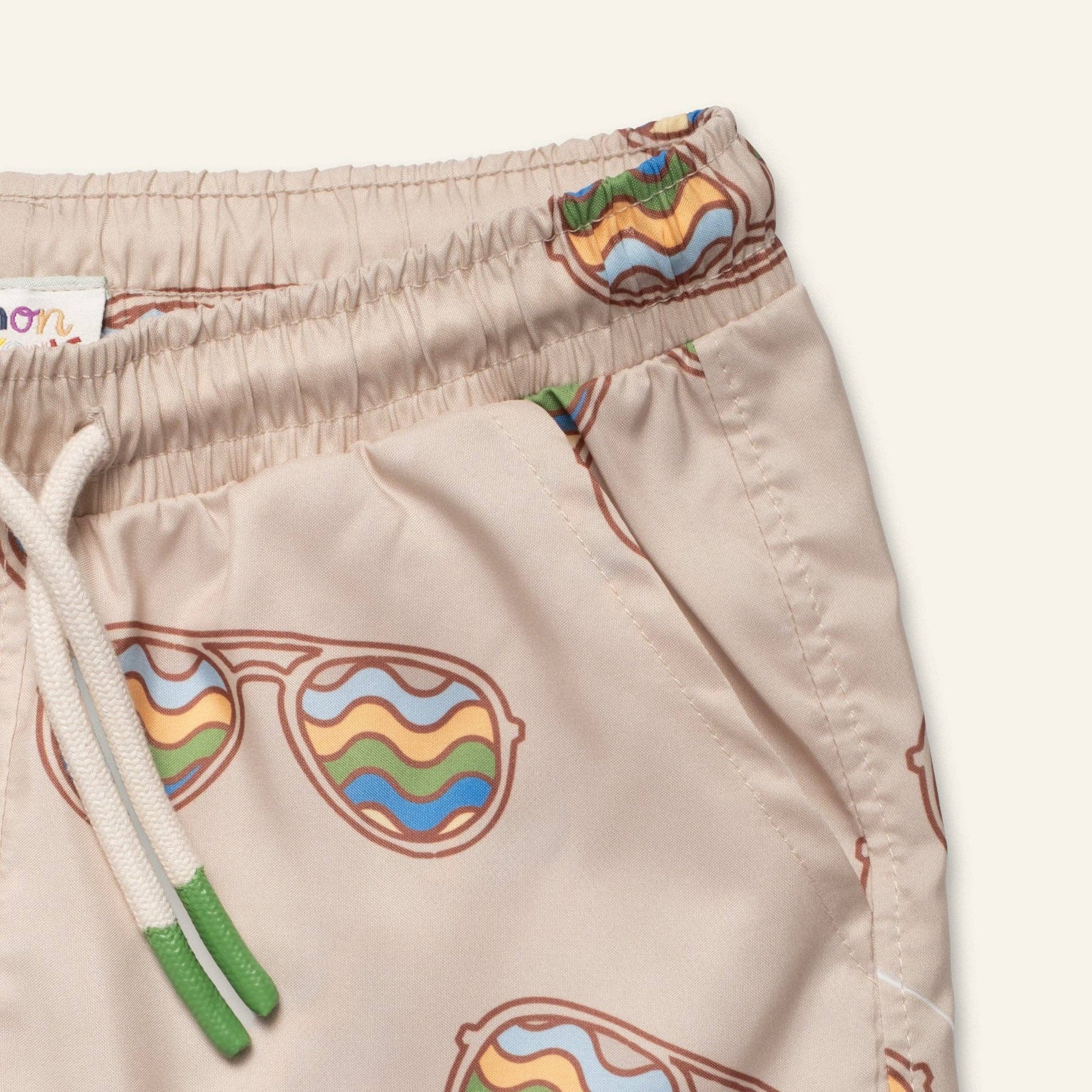Beige shorts with colorful sunglasses design and a white drawstring on a light gray background