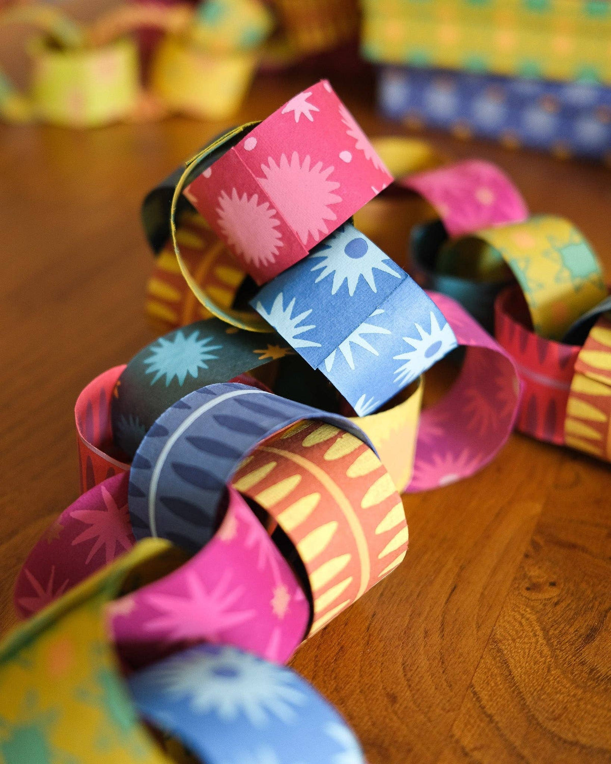 Multicolored paper chain links with sunburst and stripe patterns on a wooden table.