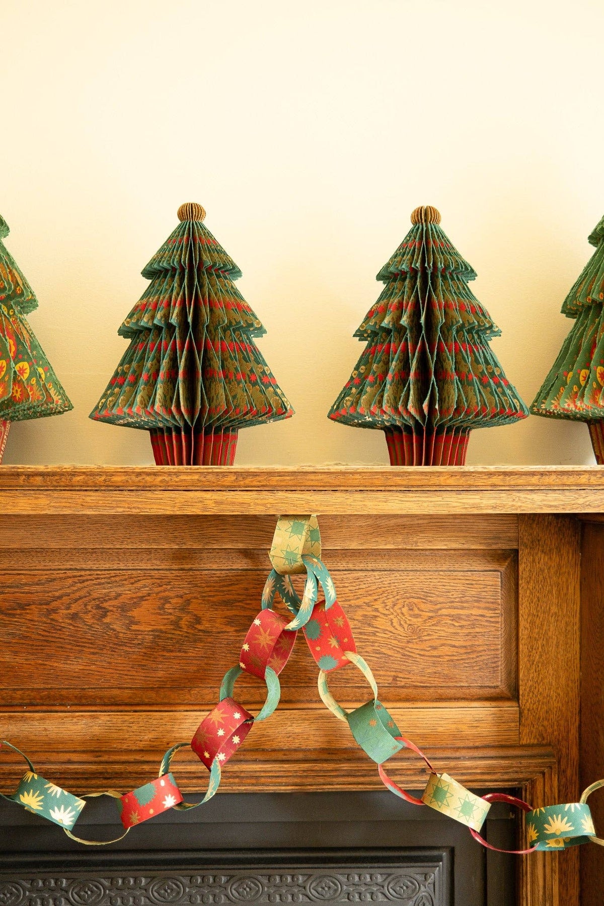 Festive red and green paper chains draped across a wooden mantel beneath honeycomb tree decorations.