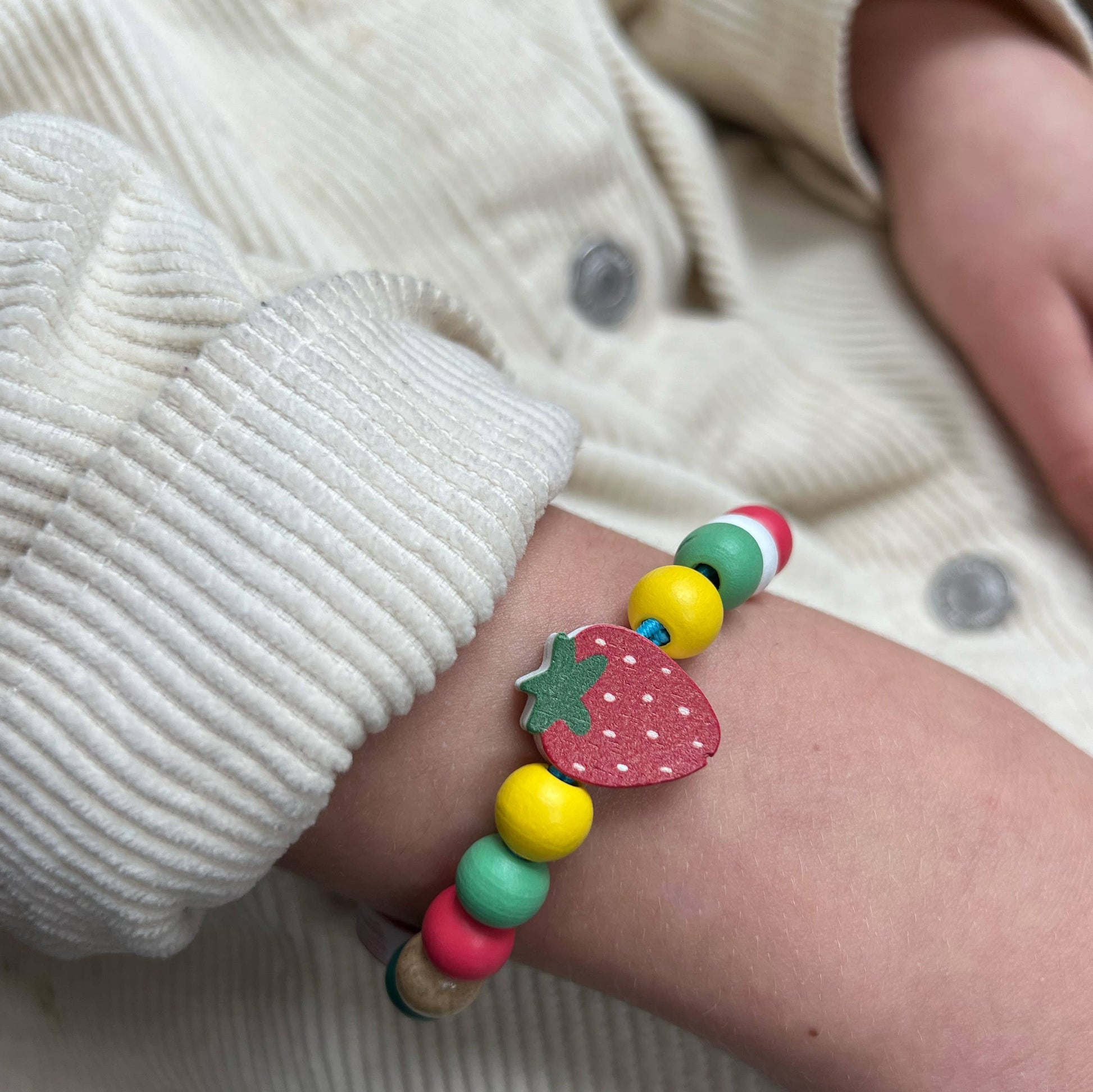 Colorful beaded bracelet with a strawberry charm on a child's wrist.