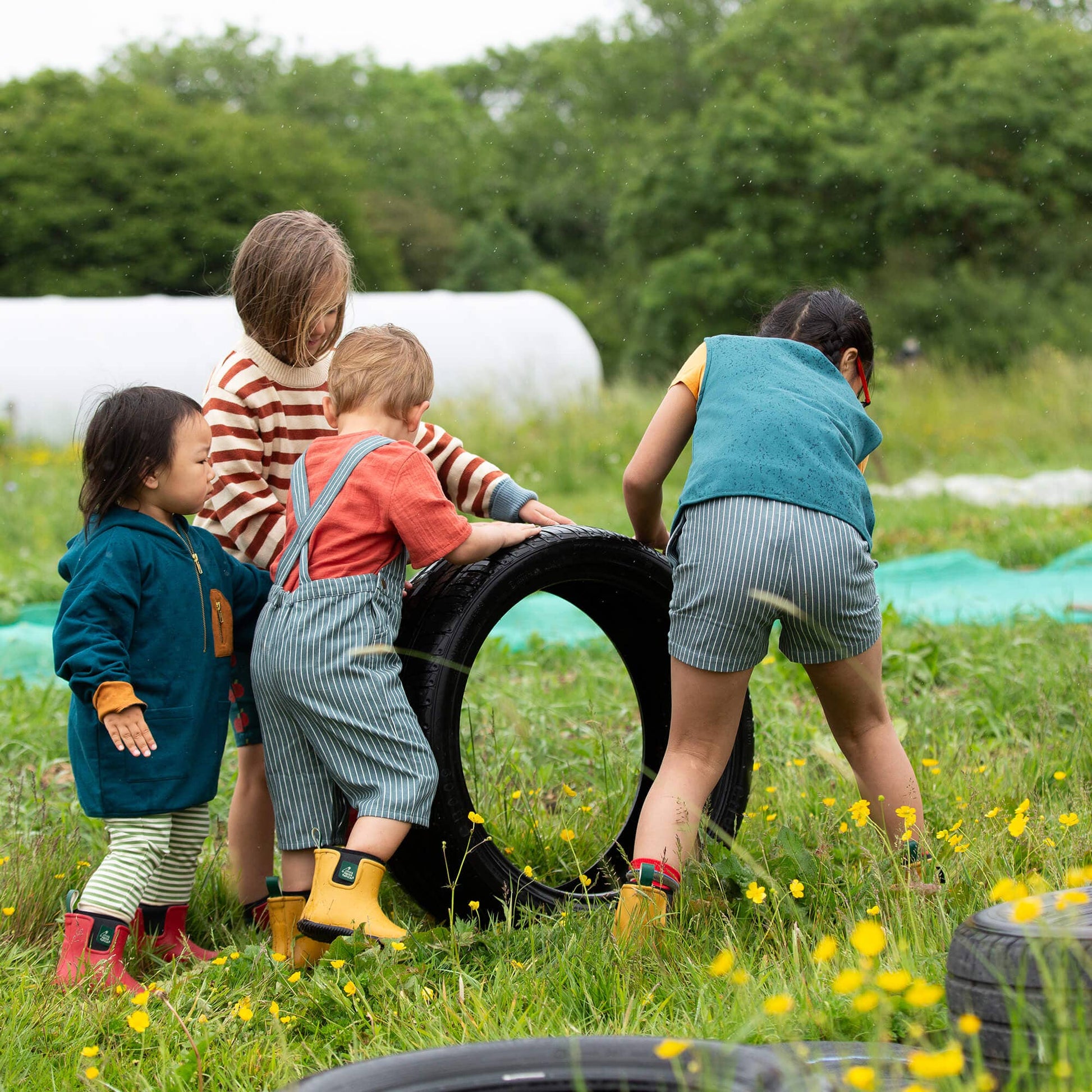 Children playing with tires in a grassy field with trees in the background