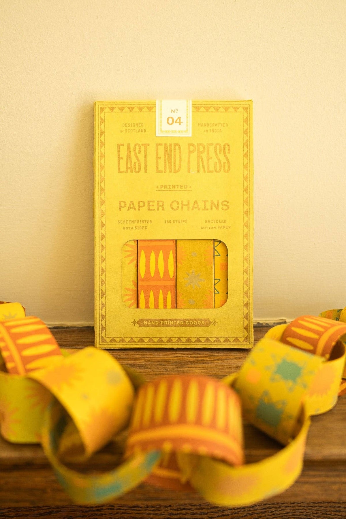 East End Press Yellow & Green Paper Chain Kit behind assembled patterned links on a wooden shelf.