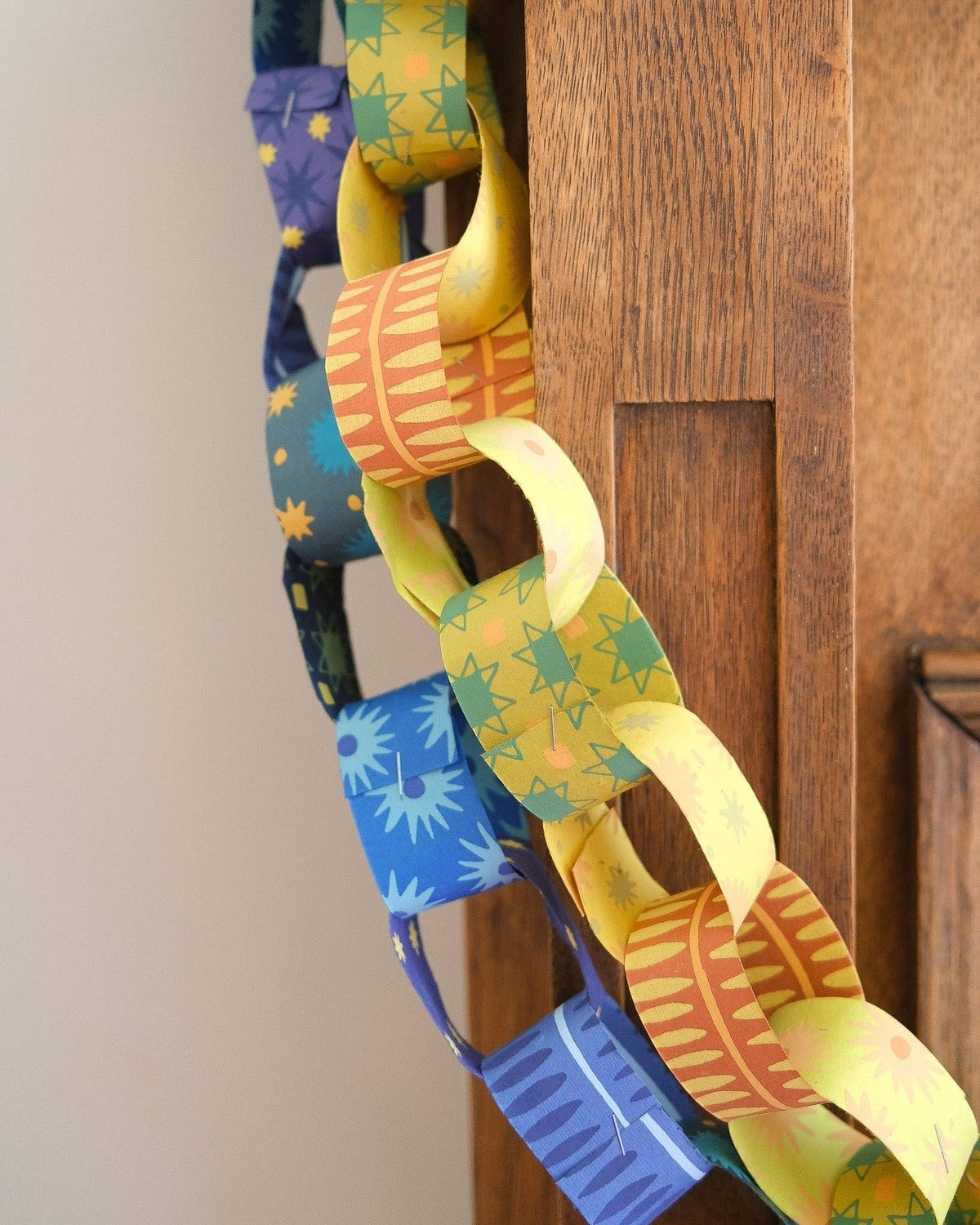 Close-up of yellow and green patterned paper links beside a blue paper chain on a wooden mantel.