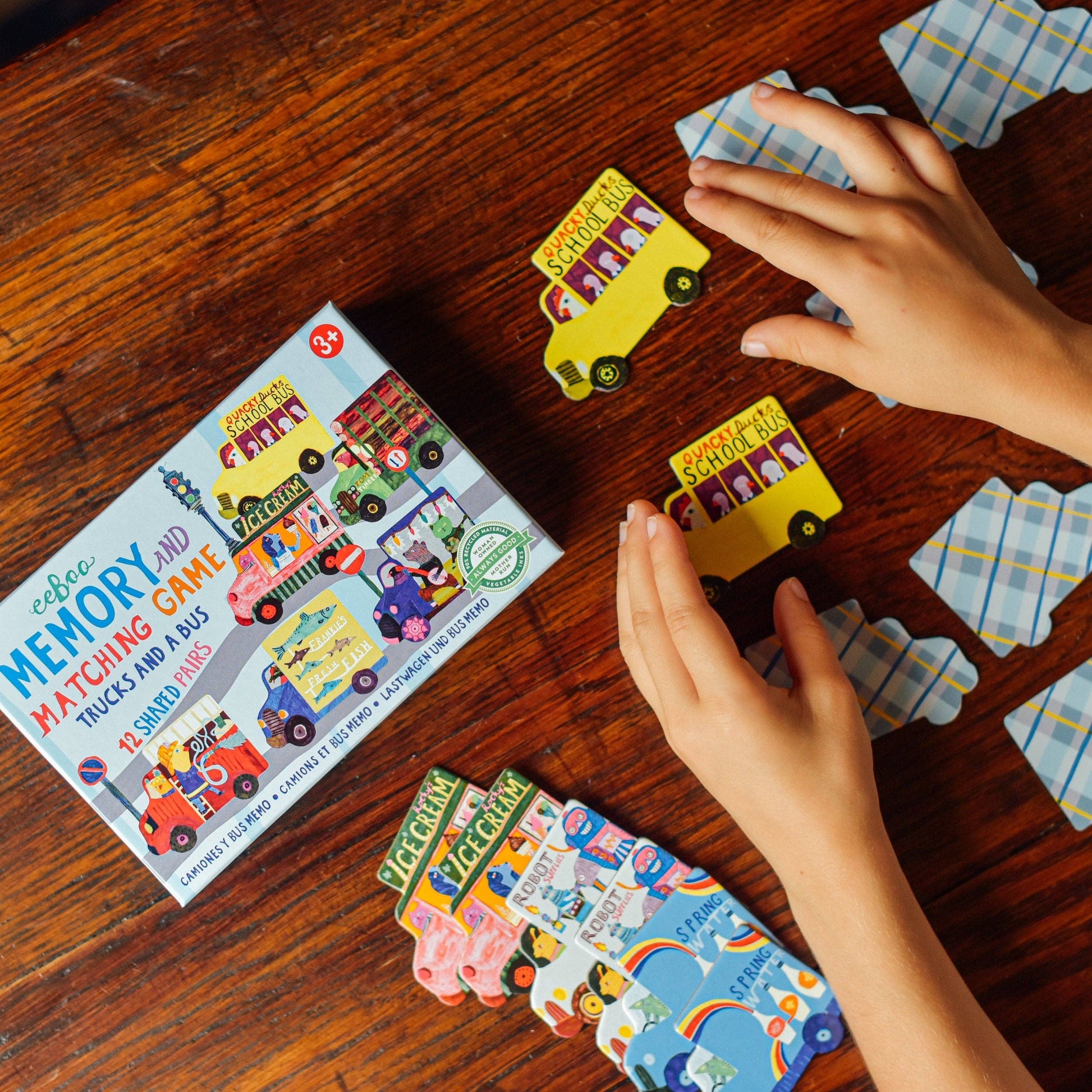 Children playing with a memory and matching game on a wooden table, featuring colorful cards and a box.