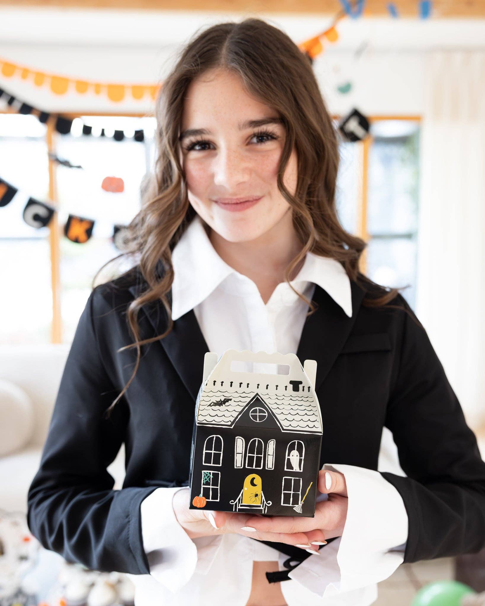 Girl holding a small house-shaped object with Halloween decorations in a classroom setting