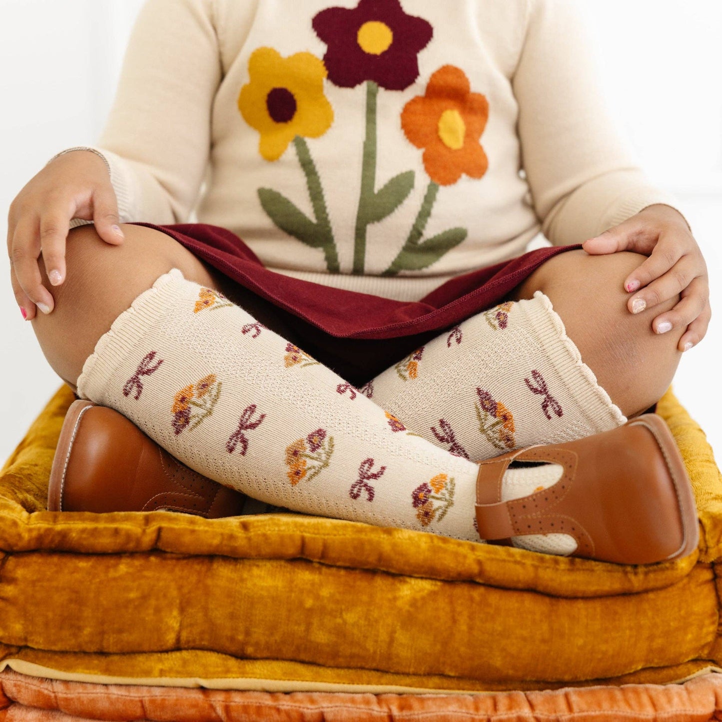 Person wearing floral-patterned socks and a sweater with flower designs, sitting on a yellow cushion.