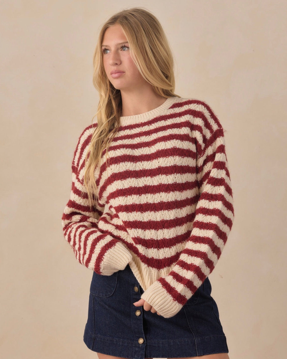 Teen wearing red and white striped long sleeve sweater and jean skirt in front of beige background