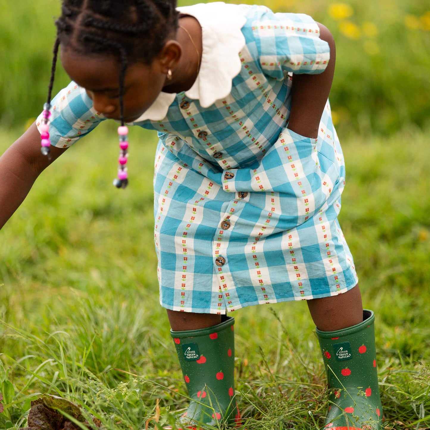 Child in a blue checkered dress and green wellies playing in a grassy field.