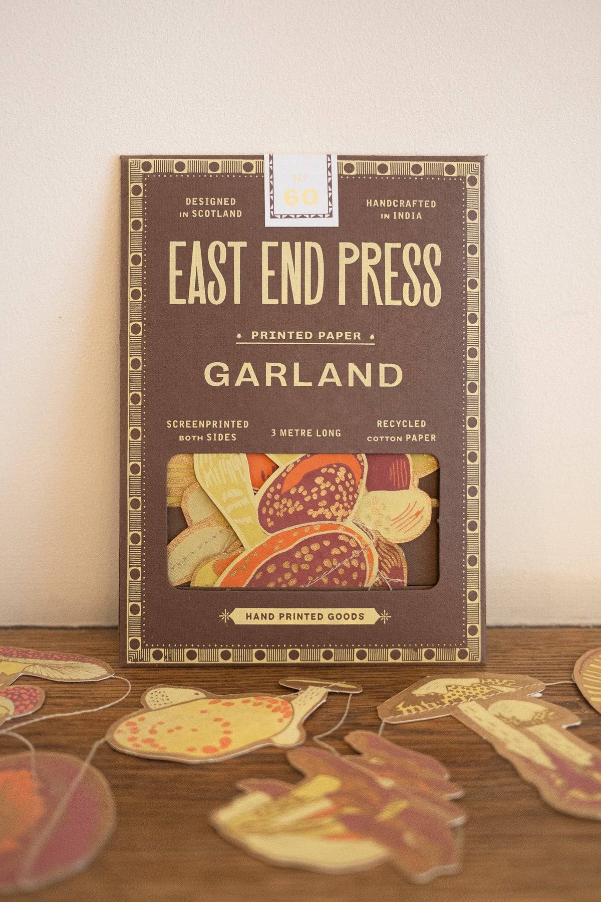 East End Press Mushroom Sewn Garland box behind colorful mushroom paper cutouts on a wooden surface.