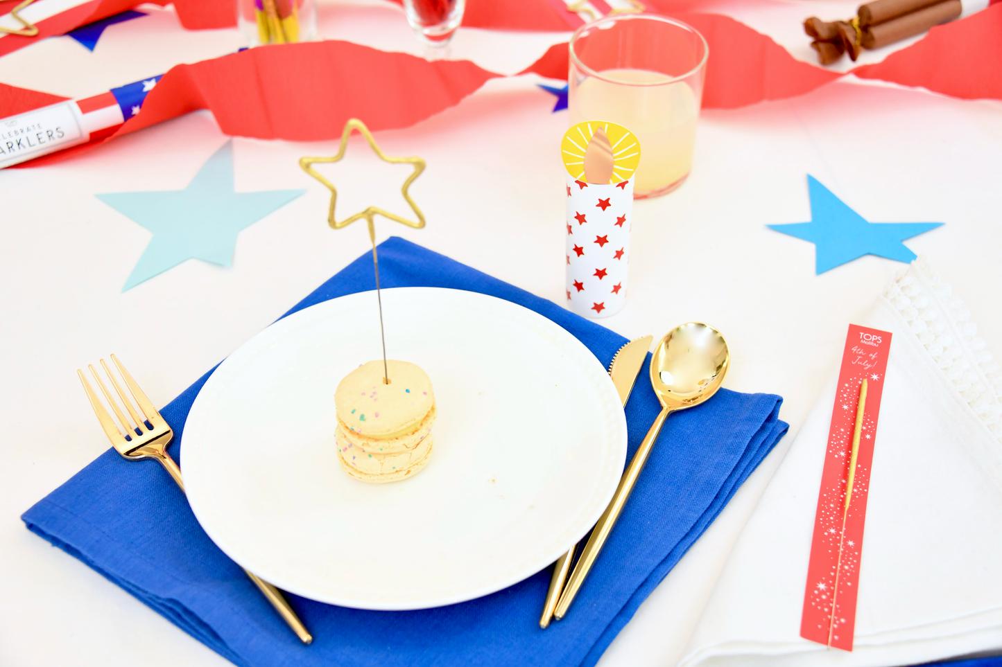 Dessert setting with a star-shaped topper on a white plate, gold fork and spoon, and red, white, and blue tablecloth.