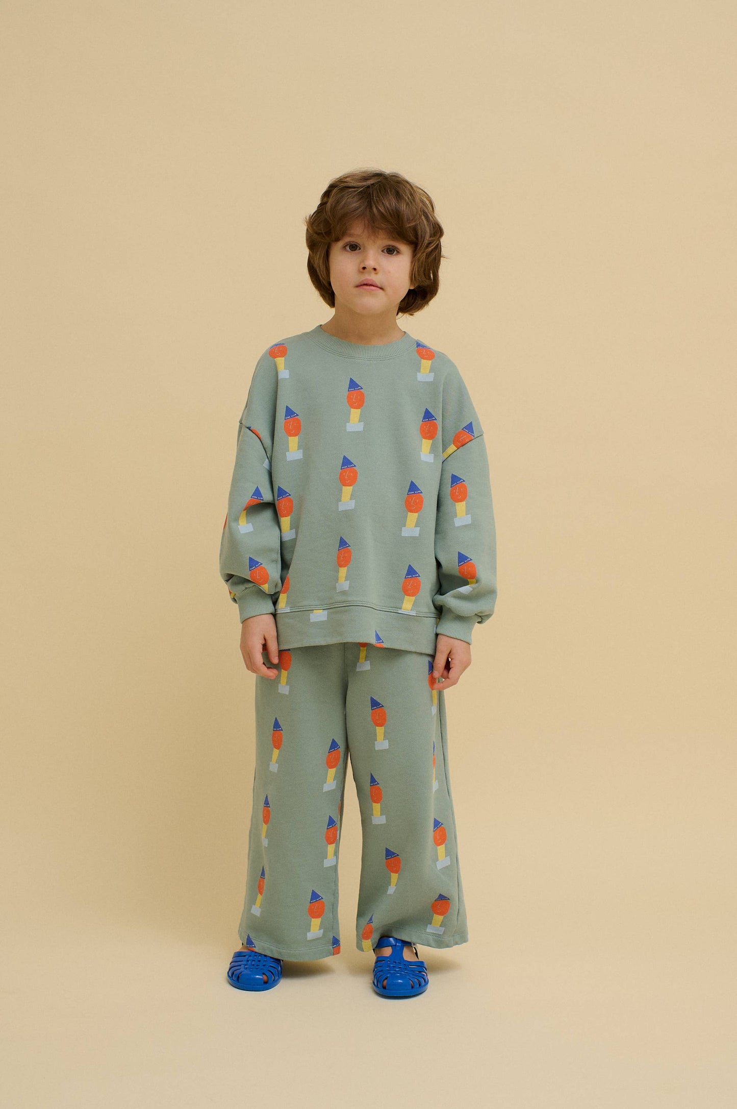 Child wearing a green outfit with colorful pattern on a beige background