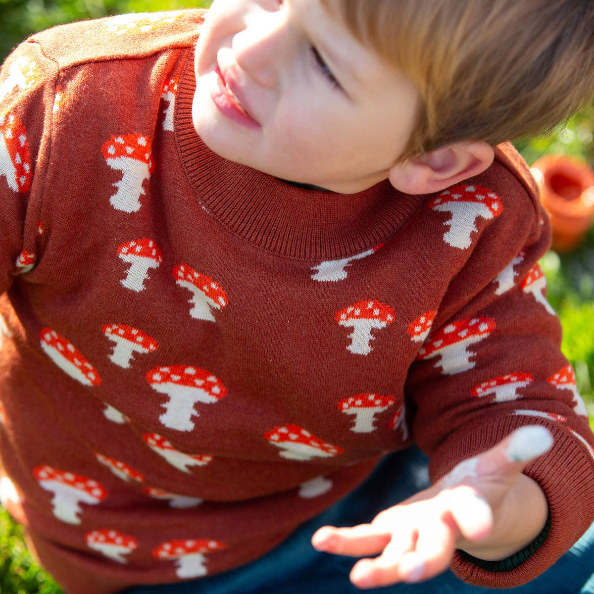 Child wearing a rust mushroom-patterned knitted jumper outdoors.