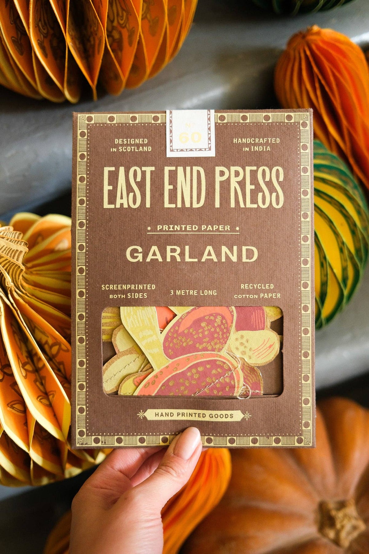 Hand holding the East End Press Mushroom Sewn Garland box in front of orange and green honeycomb pumpkins.