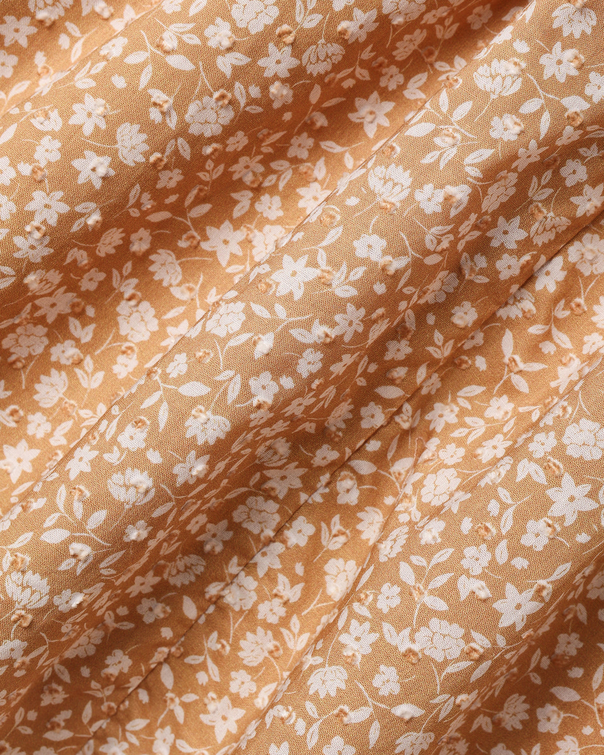 A close-up of draped fabric with a delicate white floral and leaf pattern on a warm peach-beige background.