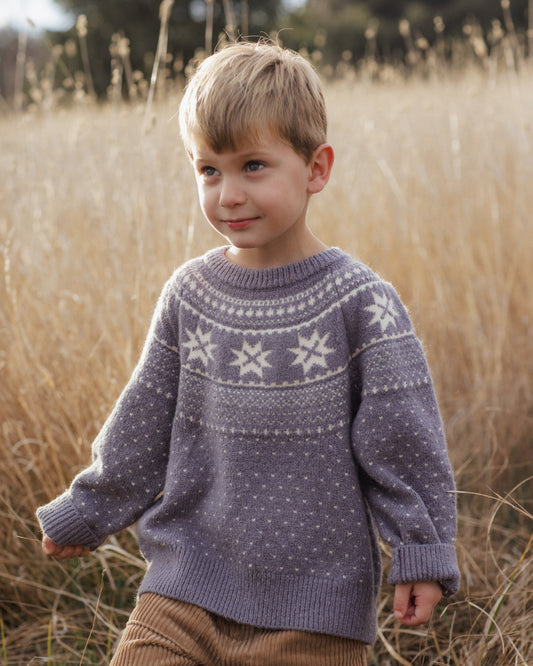 Child wearing  grey fair isle sweater and brown cords in a field of dry grass